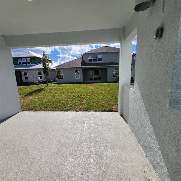 A concrete patio overlooks a grassy backyard and neighboring houses under a blue sky — 19050 BLUELEAF STREET, ORLANDO, FL