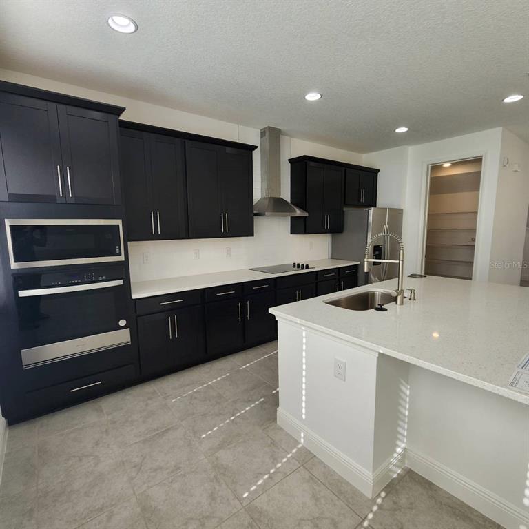 A modern kitchen features dark cabinetry, white countertops, stainless steel appliances, and a central island — 19050 BLUELEAF STREET, ORLANDO, FL