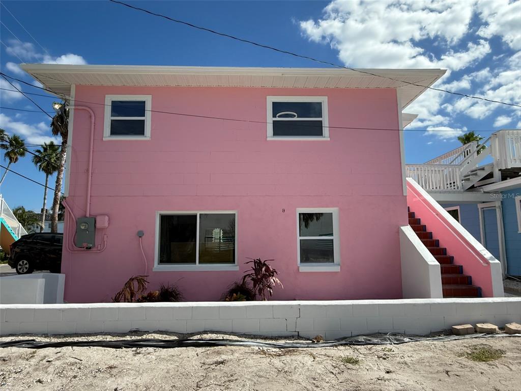 A two-story pink building with white trim and an exterior staircase sits behind a wall — 12609 SUNSHINE LANE, TREASURE ISLAND, FL
