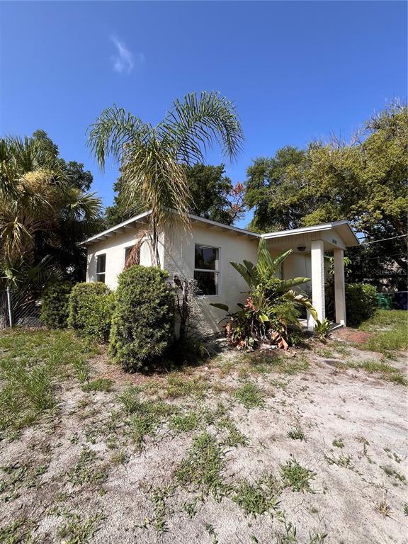 A small, light-colored house with a palm tree and overgrown landscaping under a blue sky — 3702 OHIO AVENUE, TAMPA, FL