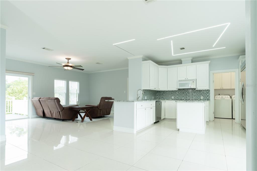 An open-concept kitchen with white cabinets and a living area with brown reclining chairs — 8345 TRILLIUM ROAD, FORT MYERS, FL