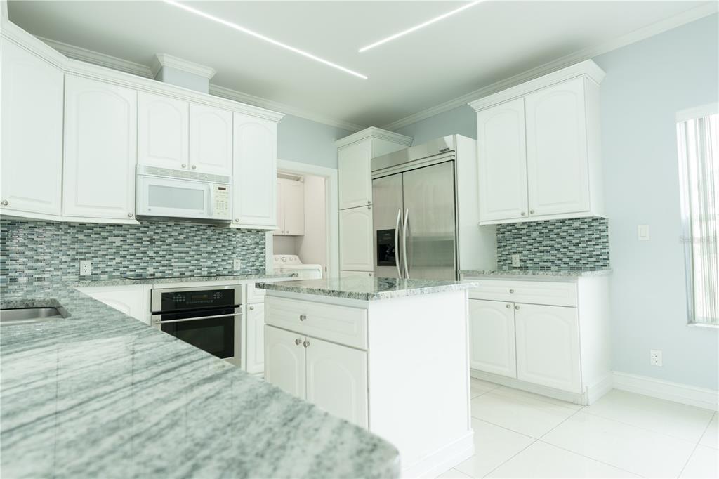 A kitchen with white cabinets, granite countertops, a center island, and a stainless steel refrigerator — 8345 TRILLIUM ROAD, FORT MYERS, FL