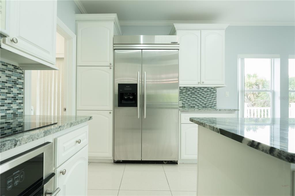 A kitchen with white cabinets, stainless steel appliances, granite countertops, and a blue tiled backsplash — 8345 TRILLIUM ROAD, FORT MYERS, FL