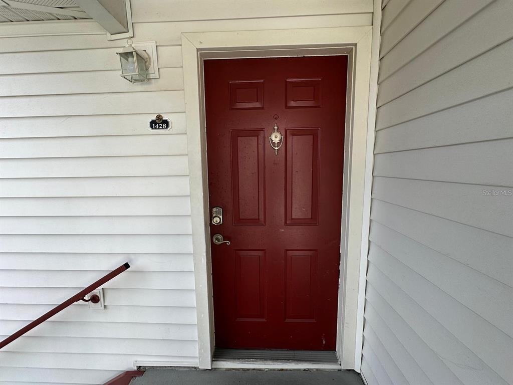 A red front door with a silver knocker is set into white horizontal siding — 11582 WESTWOOD BOULEVARD UNIT 1428, ORLANDO, FL