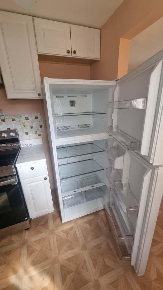 A kitchen features white cabinets, a stainless steel stove, and an open white refrigerator — 176 Piedmont D # D, Delray Beach FL 33484, DELRAY BEACH, FL