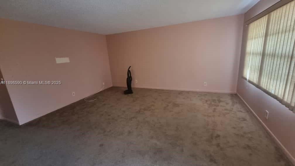 An empty room features light pink walls, beige carpeting, and vertical window blinds — 176 Piedmont D # D, Delray Beach FL 33484, DELRAY BEACH, FL