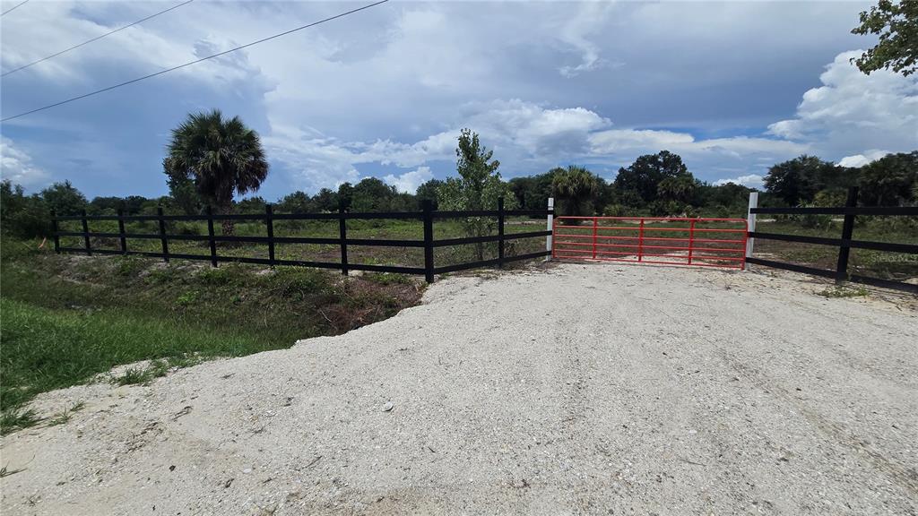 A gravel driveway leads to a red metal gate and black wooden fence on land — 21177 NW 268TH STREET, OKEECHOBEE, FL
