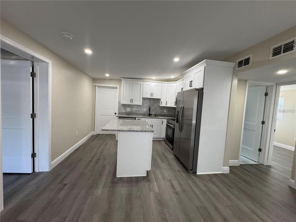 A kitchen features white cabinets, granite countertops, stainless steel appliances, and gray wood-look flooring — 7039 LENOX DRIVE, NEW PORT RICHEY, FL