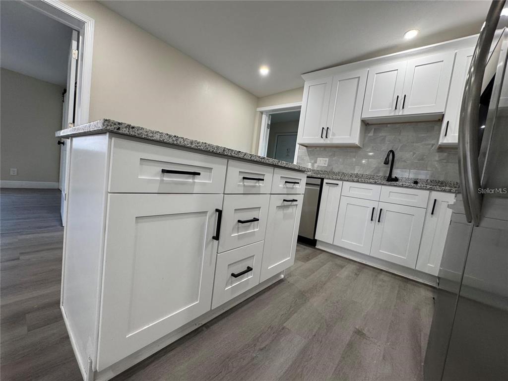 A kitchen features white cabinets, granite countertops, a center island, and wood-look flooring — 7039 LENOX DRIVE, NEW PORT RICHEY, FL
