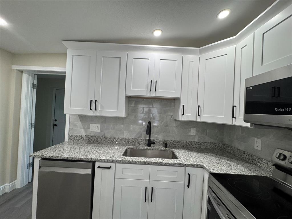 A kitchen features white cabinets, granite countertops, a stainless steel sink, and a subway tile backsplash — 7039 LENOX DRIVE, NEW PORT RICHEY, FL