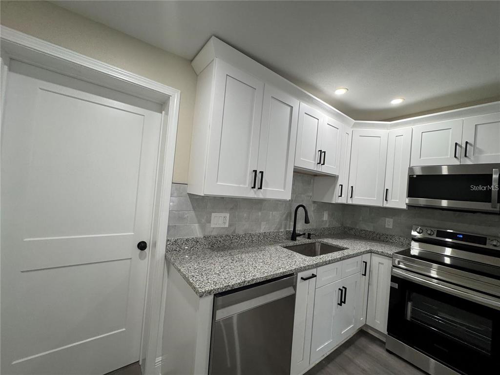 A kitchen features white cabinets, granite countertops, stainless steel appliances, and a gray backsplash — 7039 LENOX DRIVE, NEW PORT RICHEY, FL