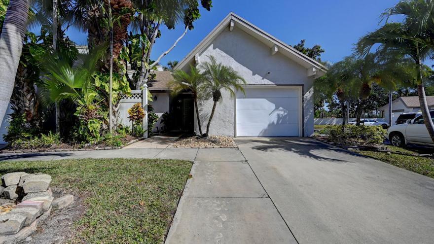 A single-story house with a white garage door, a concrete driveway, and surrounding palm trees — 6660 Canary Palm Circle, Boca Raton FL 33433, BOCA RATON, FL