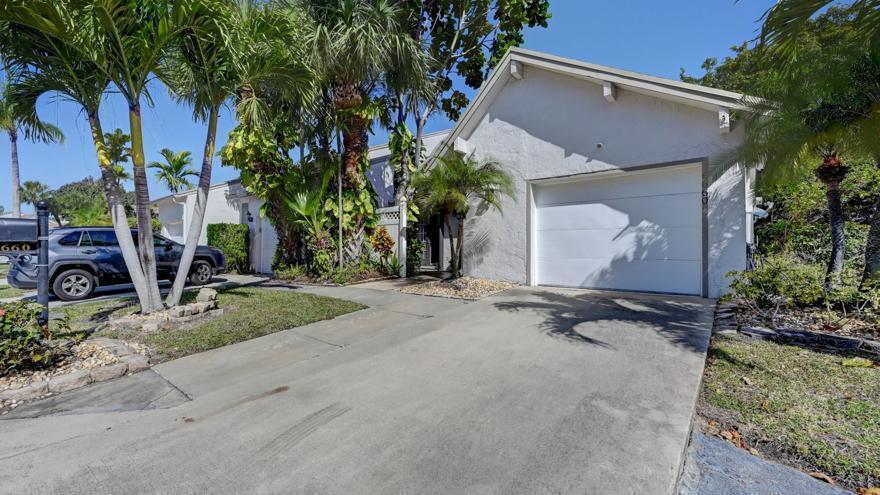 A white house with a garage and palm trees sits behind a concrete driveway — 6660 Canary Palm Circle, Boca Raton FL 33433, BOCA RATON, FL