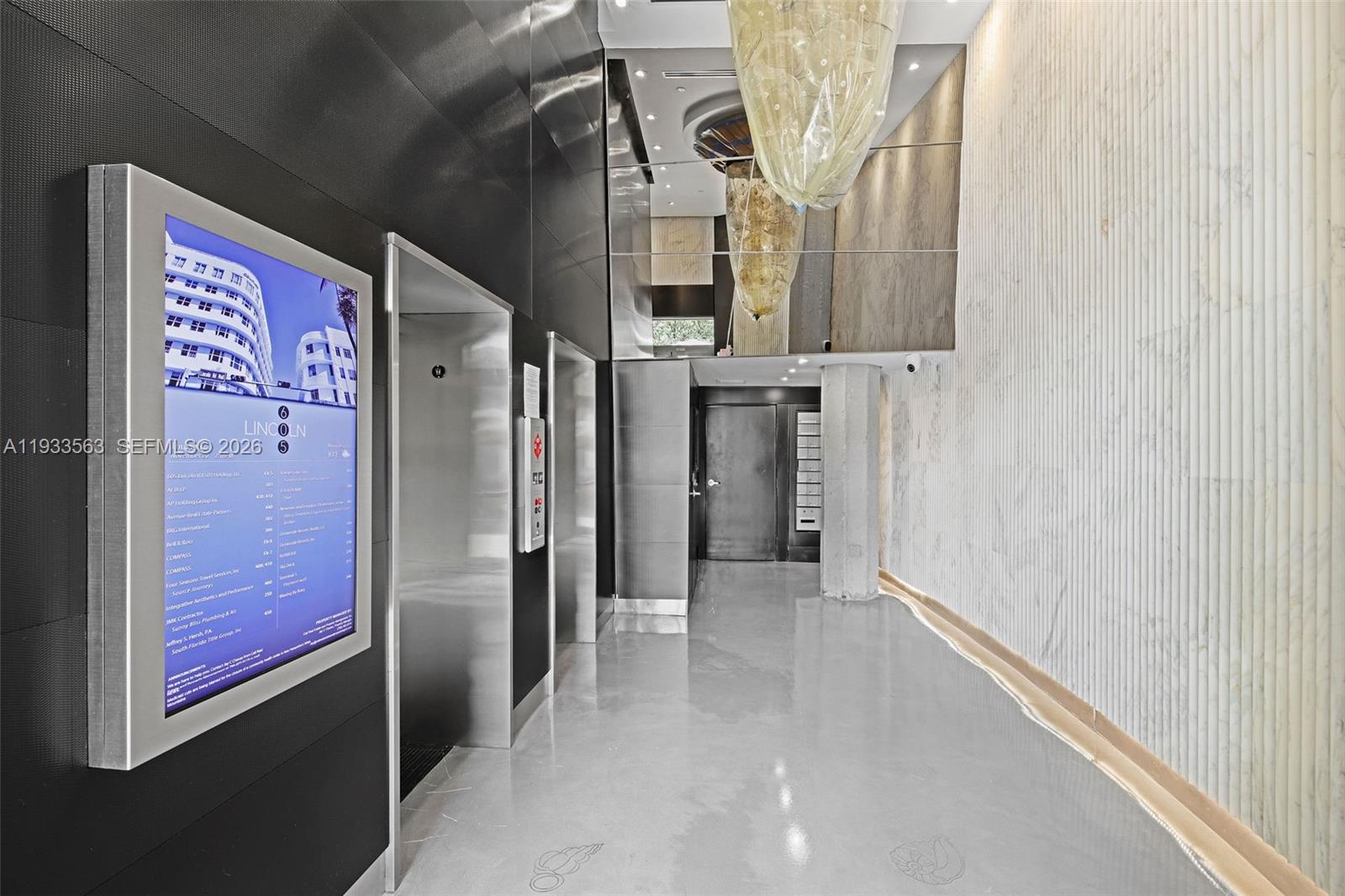 A modern building lobby features a digital directory, stainless steel elevators, and textured wall panels — 605 Lincoln Rd # 500, Miami Beach FL 33139, MIAMI BEACH, FL