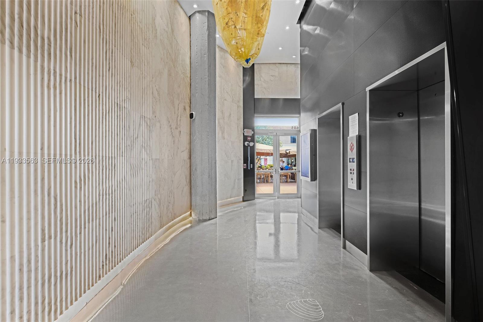 A modern building lobby features a textured stone wall, polished floors, and stainless steel elevators — 605 Lincoln Rd # 500, Miami Beach FL 33139, MIAMI BEACH, FL