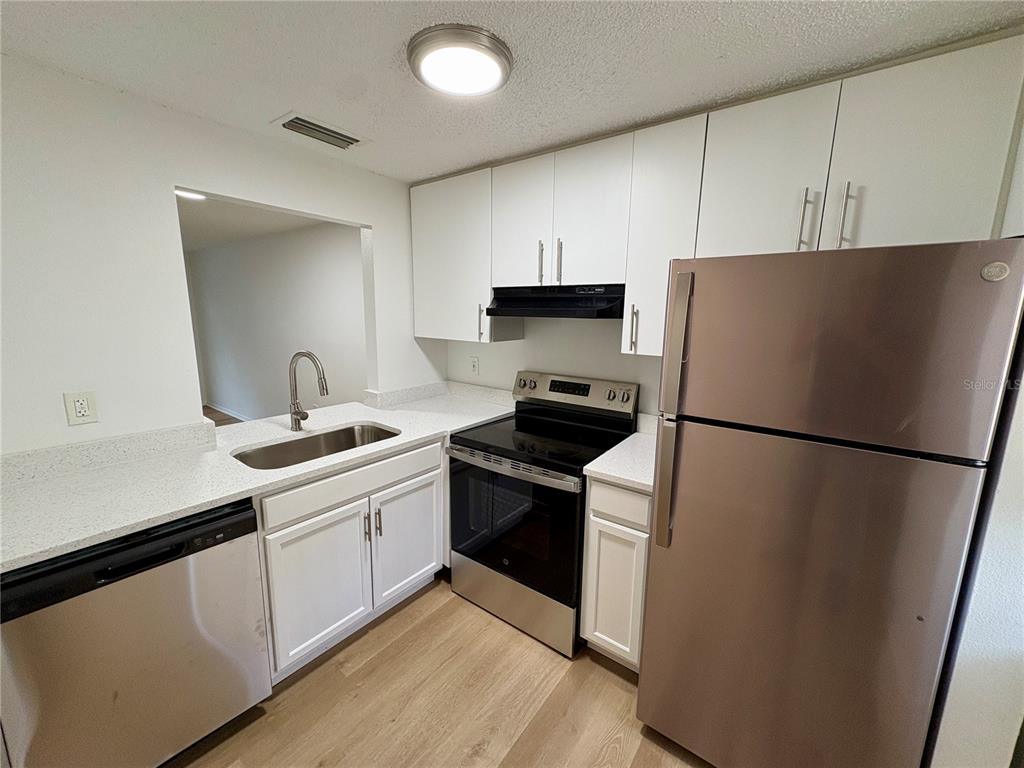 A kitchen features white cabinets, stainless steel appliances, a sink, and light-colored countertops — 408 57TH AVENUE DRIVE E UNIT C, BRADENTON, FL