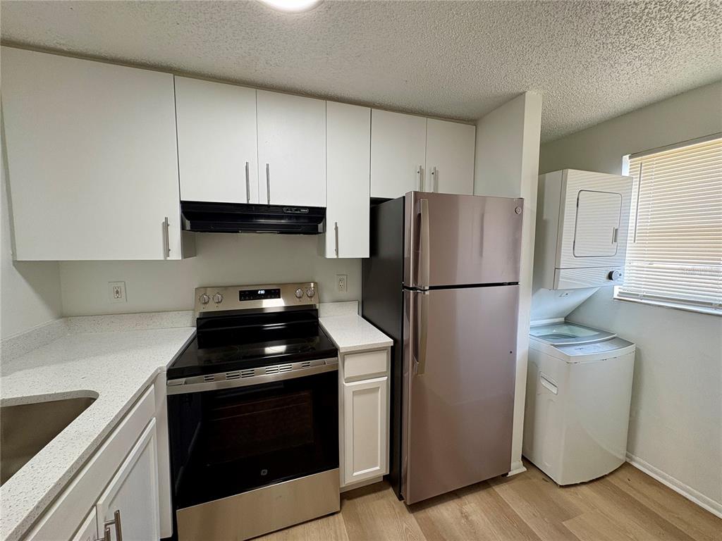 A kitchen featuring white cabinets, stainless steel appliances, and a stacked washer and dryer unit — 408 57TH AVENUE DRIVE E UNIT C, BRADENTON, FL