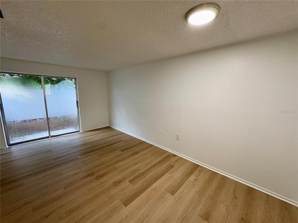 An empty room features light wood-look flooring, white walls, and a sliding glass door — 408 57TH AVENUE DRIVE E UNIT C, BRADENTON, FL