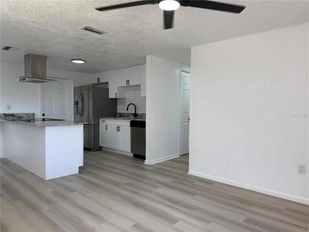 A kitchen with white cabinets, granite countertops, and stainless steel appliances opens to a living area — 3821 AVENUE J NW, WINTER HAVEN, FL