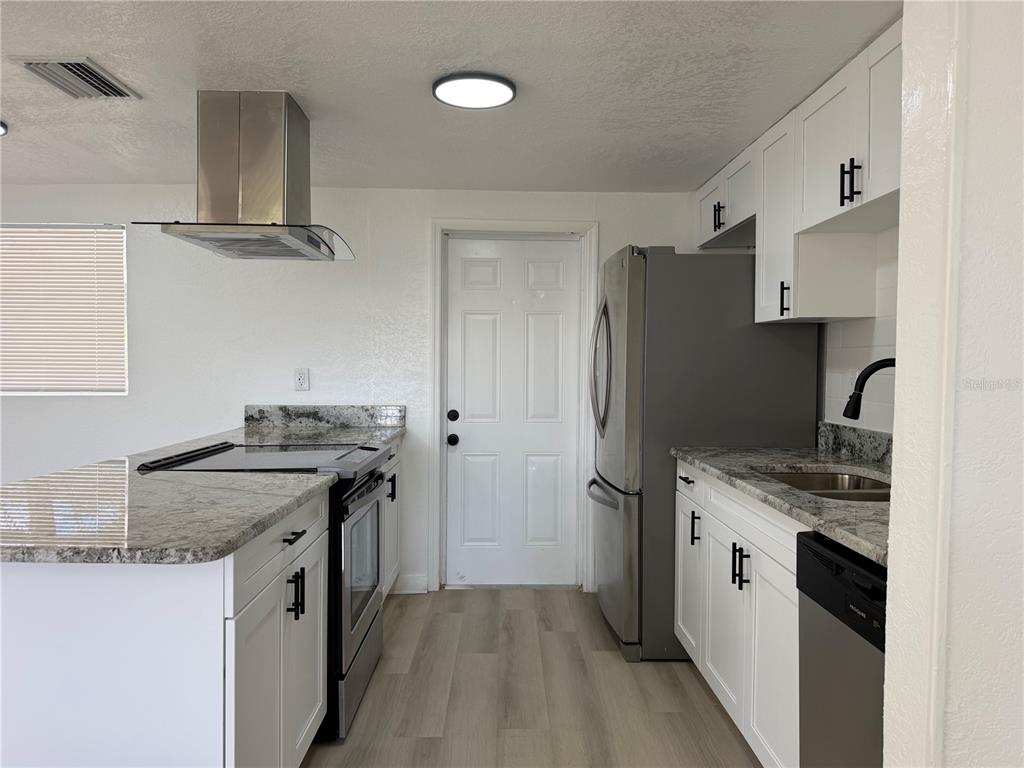 A kitchen features white cabinets, granite countertops, stainless steel appliances, and light wood-look flooring — 3821 AVENUE J NW, WINTER HAVEN, FL