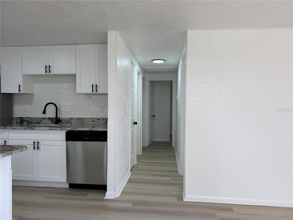 A kitchen with white cabinets and a stainless steel dishwasher leads into a hallway — 3821 AVENUE J NW, WINTER HAVEN, FL