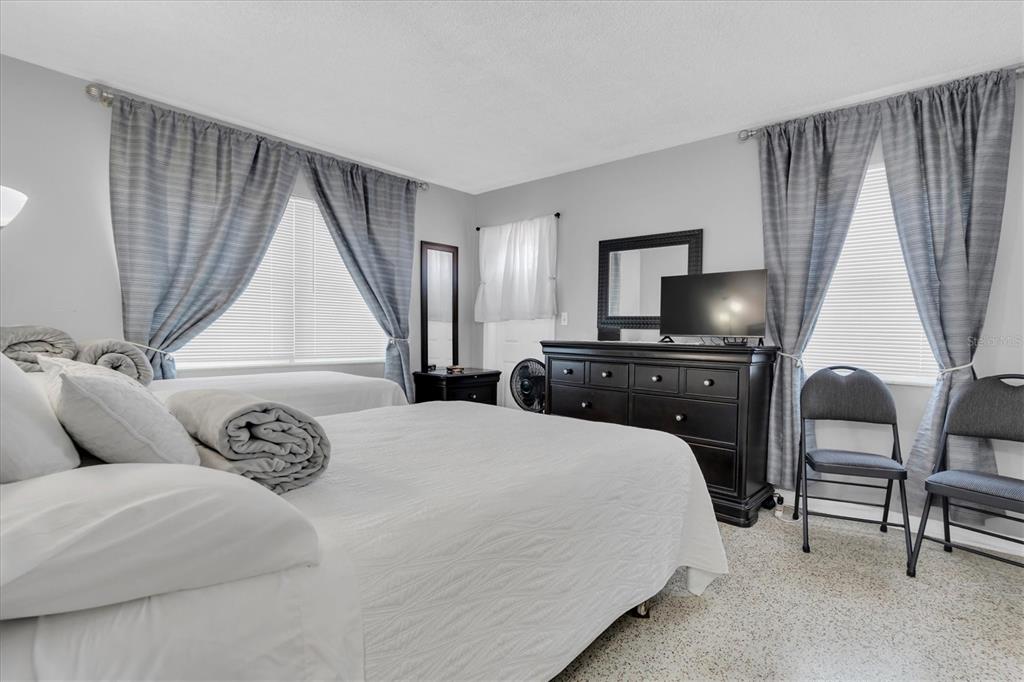 A bedroom features two beds, a dark wood dresser with a television, and gray curtains — 121 46TH AVENUE UNIT 2A, ST PETE BEACH, FL