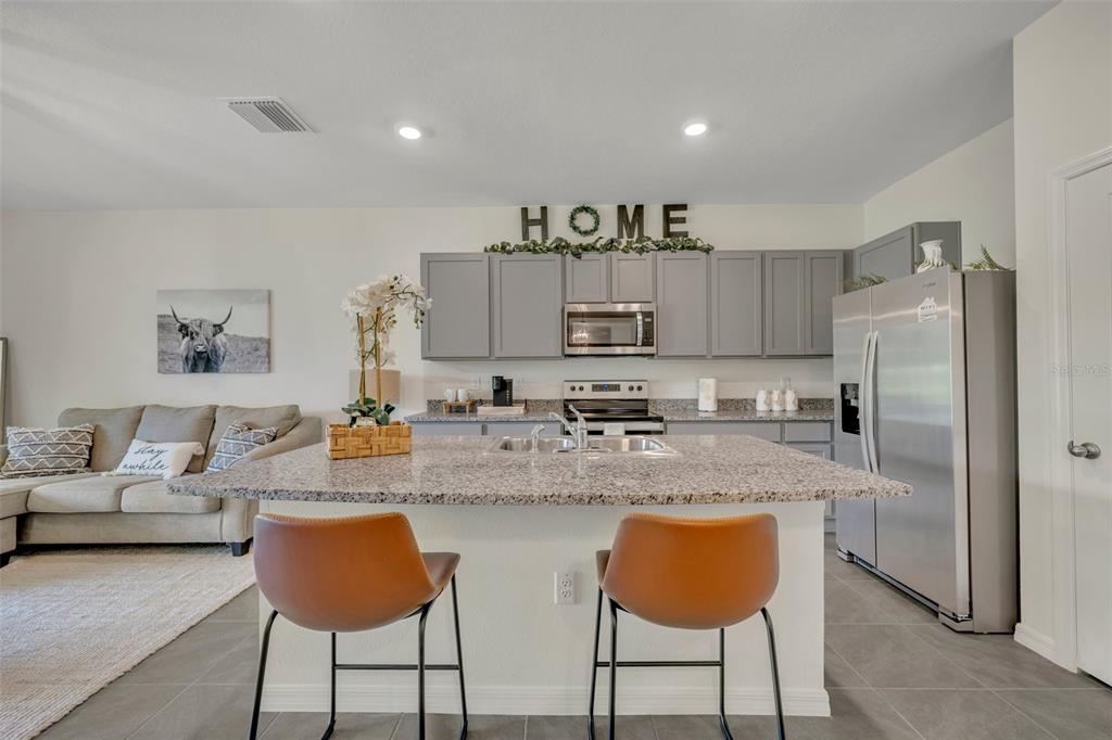 A kitchen with gray cabinets, granite countertops, and an island with two brown bar stools — 3534 MARIGOLD PATCH COURT, PLANT CITY, FL