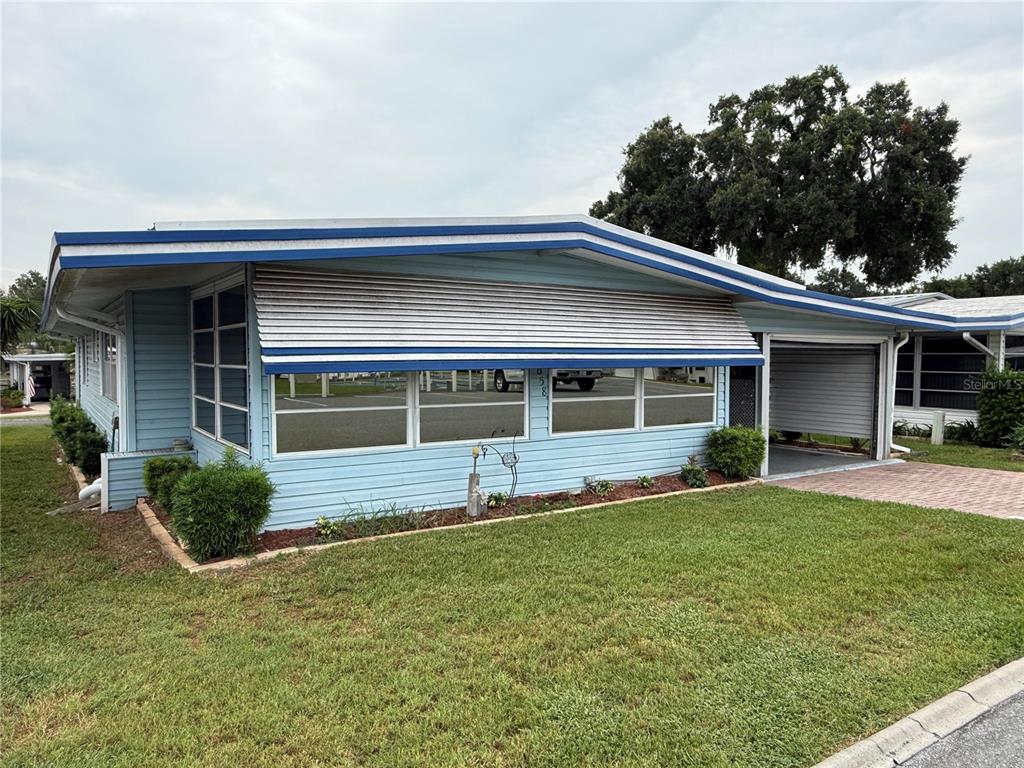 A light blue mobile home with a carport and metal window awnings sits on grass — 658 MISTI DRIVE, LEESBURG, FL