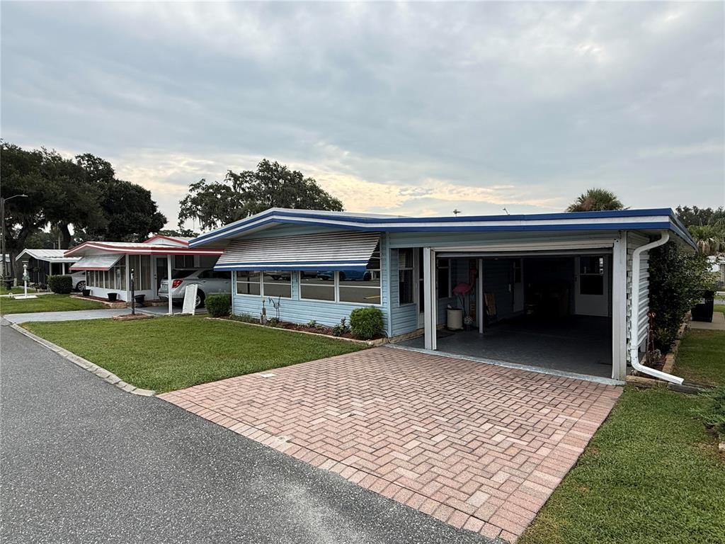 A light blue mobile home features a brick driveway and a covered carport — 658 MISTI DRIVE, LEESBURG, FL