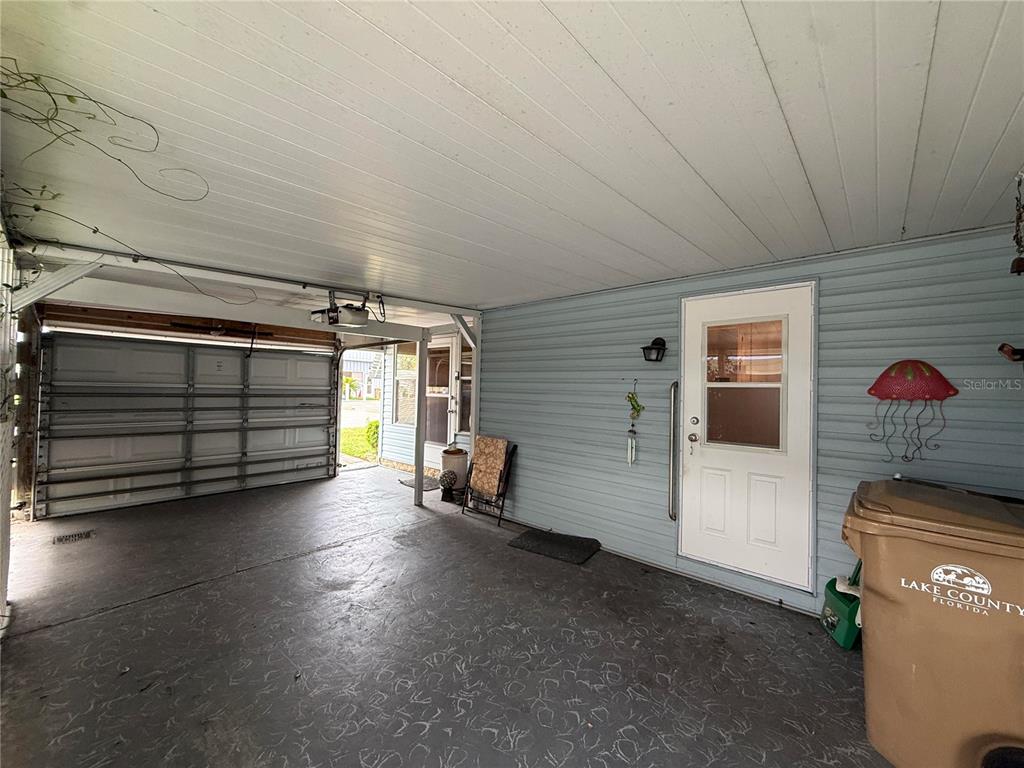 A covered carport with a concrete floor, a white door, and a garage door entrance — 658 MISTI DRIVE, LEESBURG, FL