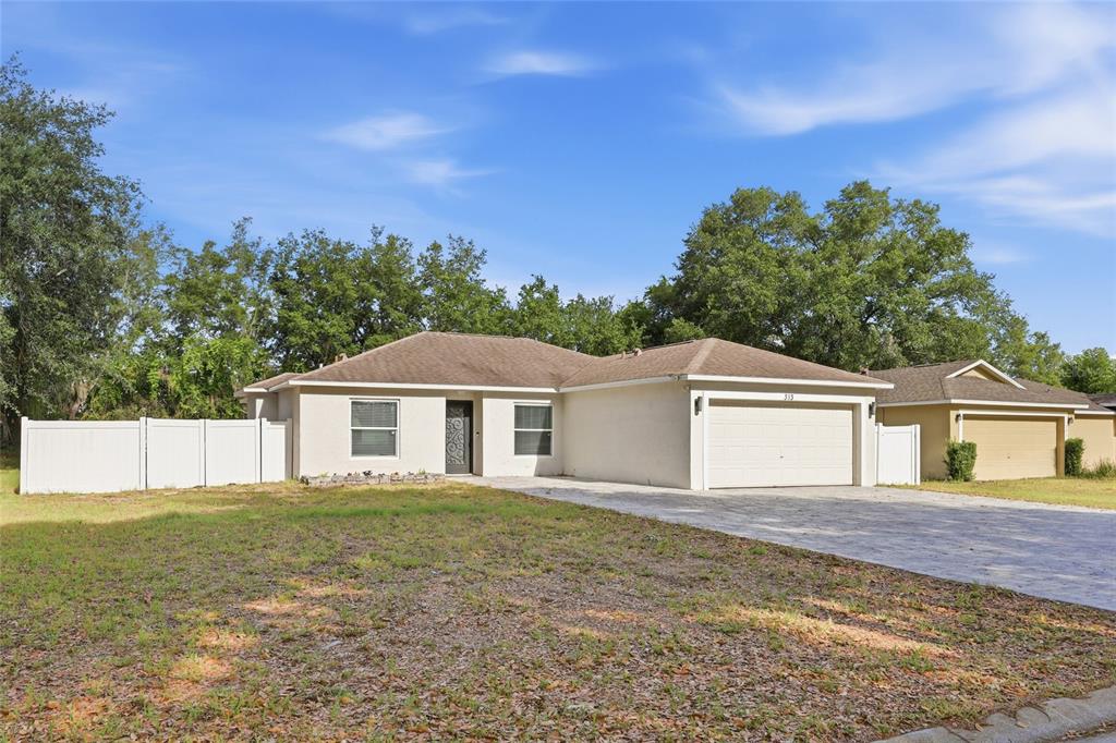 A single-story house with a beige stucco exterior, a two-car garage, and a white fence — 313 FOGGY CREEK ROAD, DAVENPORT, FL