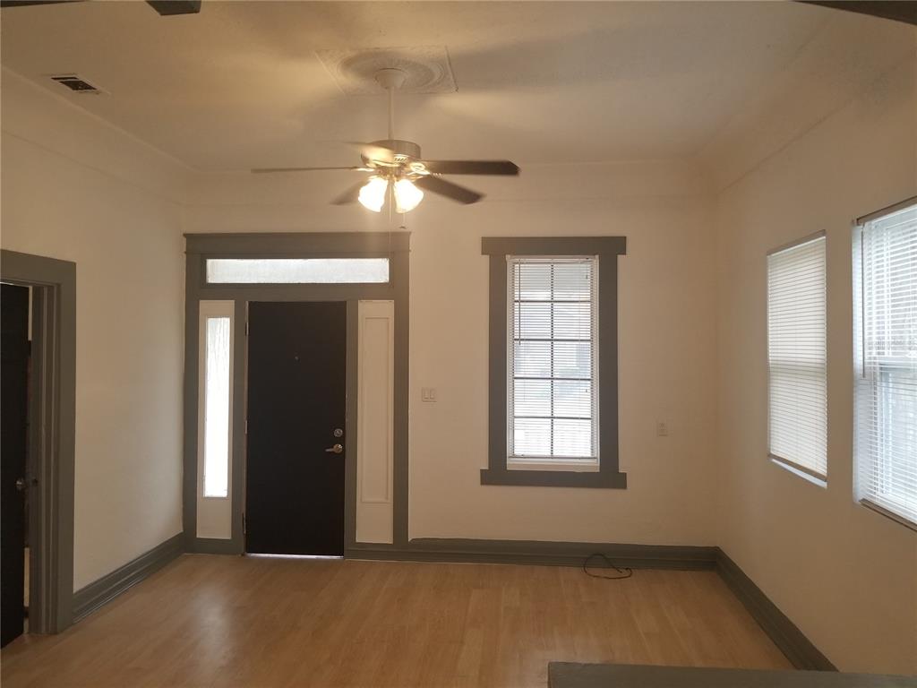 A living room features light wood flooring, gray trim, a ceiling fan, and a black door — 2107 W CHESTNUT STREET, TAMPA, FL