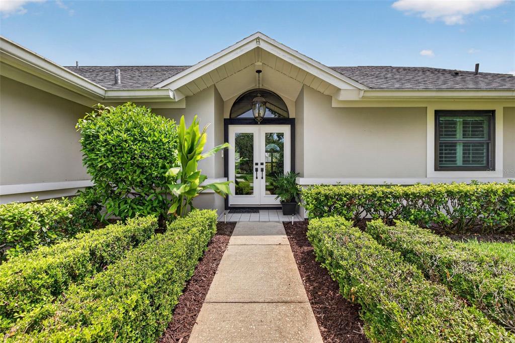 A concrete walkway leads to the double front doors of a house with landscaped hedges — 2604 ROYAL LIVERPOOL DRIVE, TARPON SPRINGS, FL