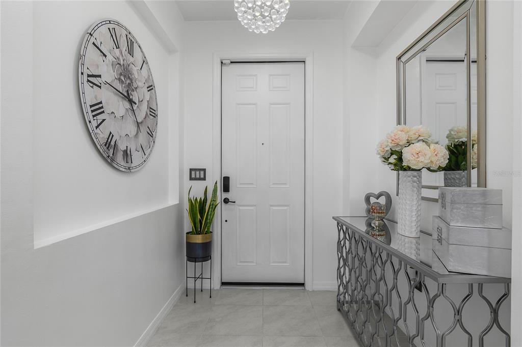 A bright entryway features a large wall clock, a mirrored console table, and a white door — 4834 CORRADO WAY, AVE MARIA, FL