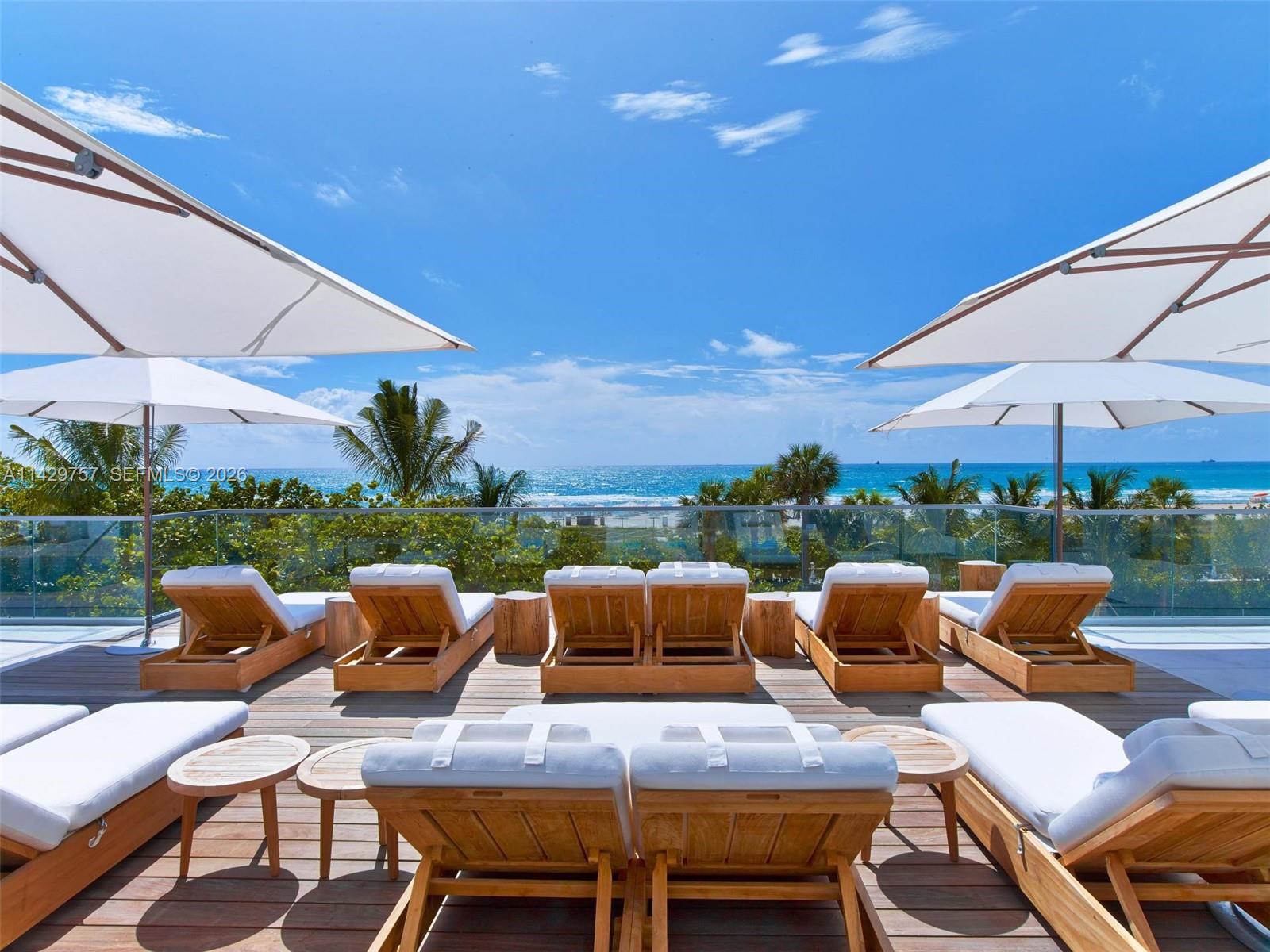 A living room features a gray armchair, a white media console, and a balcony with ocean views — 102 24th St # 1013, Miami Beach FL 33139, MIAMI BEACH, FL