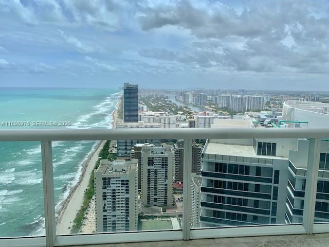 A high-angle view from a balcony overlooks a sandy beach, the ocean, and city buildings — 1830 S Ocean Dr # 4904, Hallandale Beach FL 33009, HALLANDALE BEACH, FL