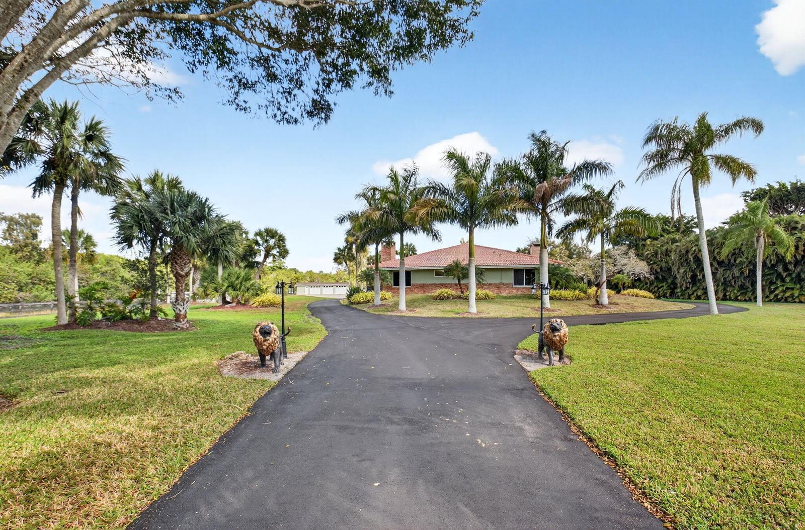 A paved driveway leads to a house with palm trees and two lion statues — 10965 La Reina Road, Delray Beach FL 33446, DELRAY BEACH, FL