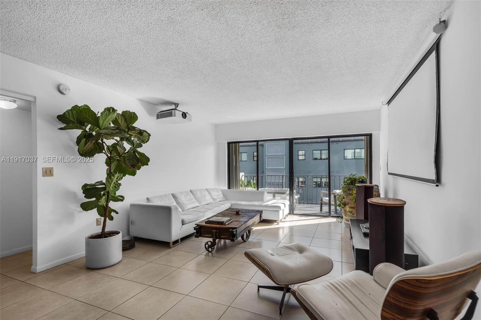 A living room features a white sectional sofa, a projector, a screen, and tile flooring — 575 Crandon Blvd # 504, Key Biscayne FL 33149, KEY BISCAYNE, FL