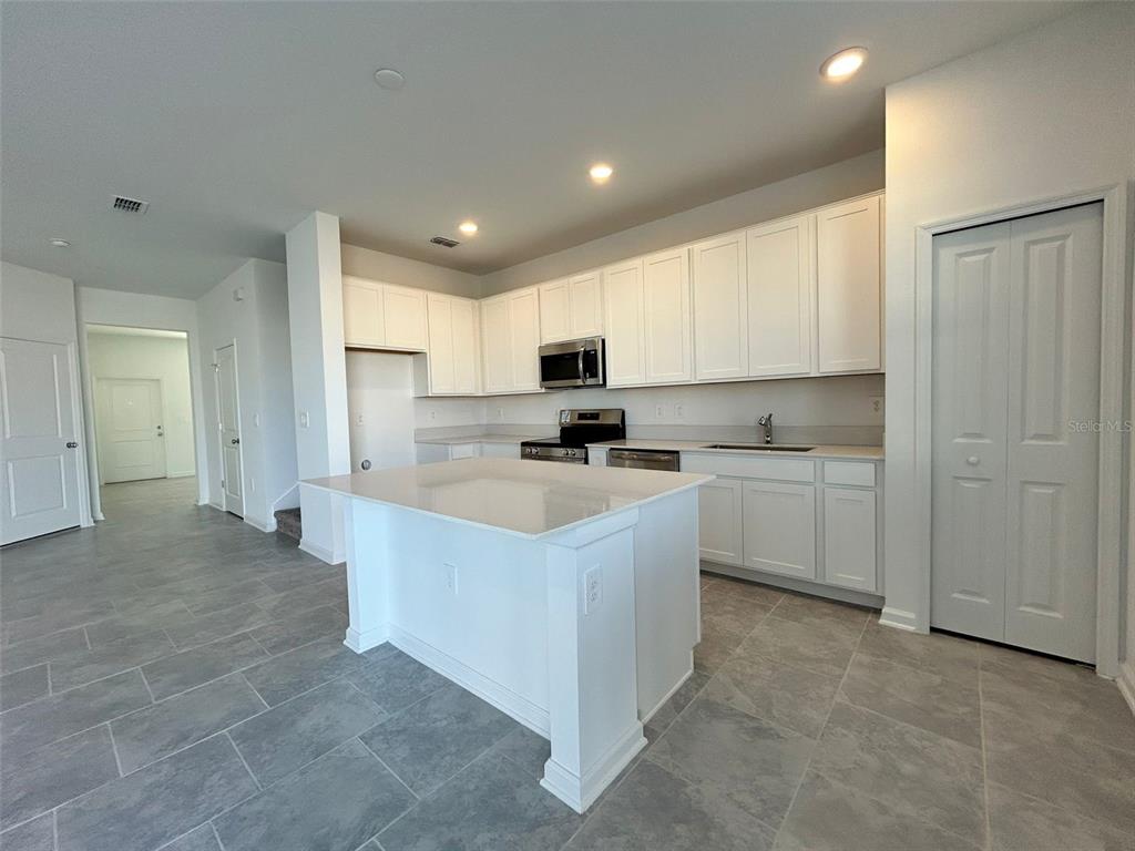A kitchen features white cabinets, a central island, and gray tile flooring — 3019 CHANTILLY DRIVE, DAVENPORT, FL