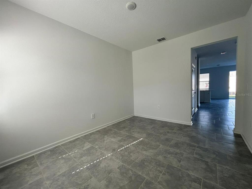An empty room with gray tile flooring and white walls leads into a hallway — 3019 CHANTILLY DRIVE, DAVENPORT, FL