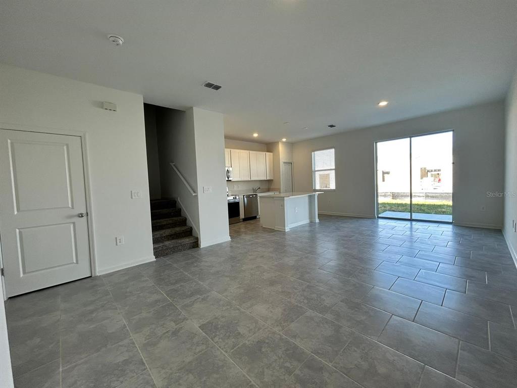 An open-concept living area features gray tile flooring, a kitchen with white cabinets, and stairs — 3019 CHANTILLY DRIVE, DAVENPORT, FL