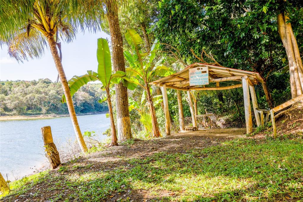 A wooden gazebo sits on a grassy bank overlooking a river near lush trees — KM 22.1 CARR 119, SAN SEBASTIAN, PR