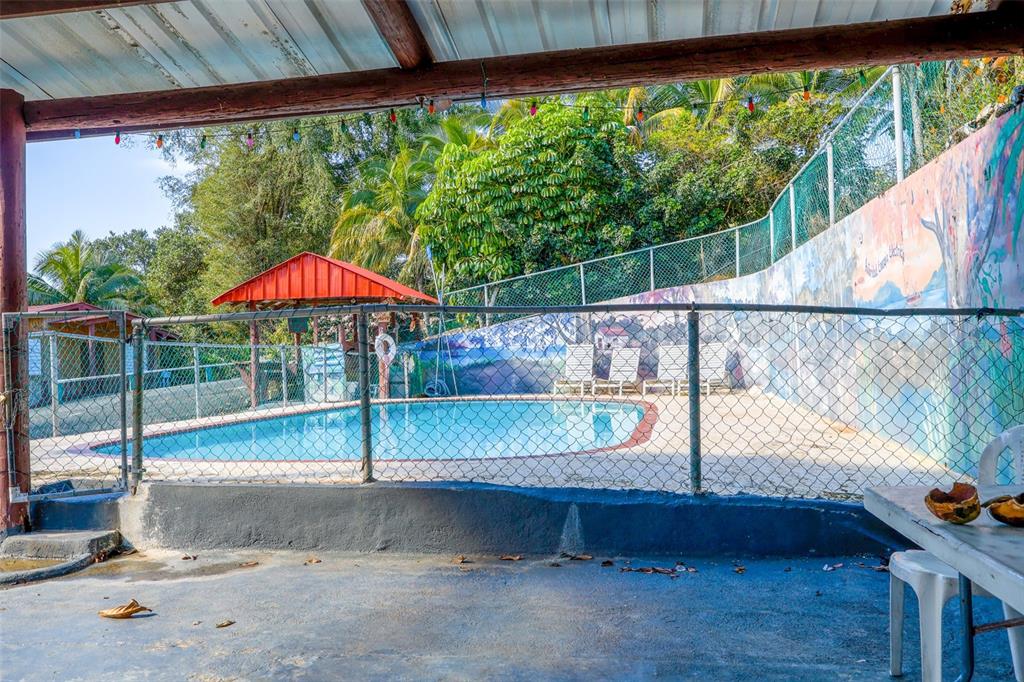 A fenced-in swimming pool sits outdoors next to a painted wall and a covered patio — KM 22.1 CARR 119, SAN SEBASTIAN, PR