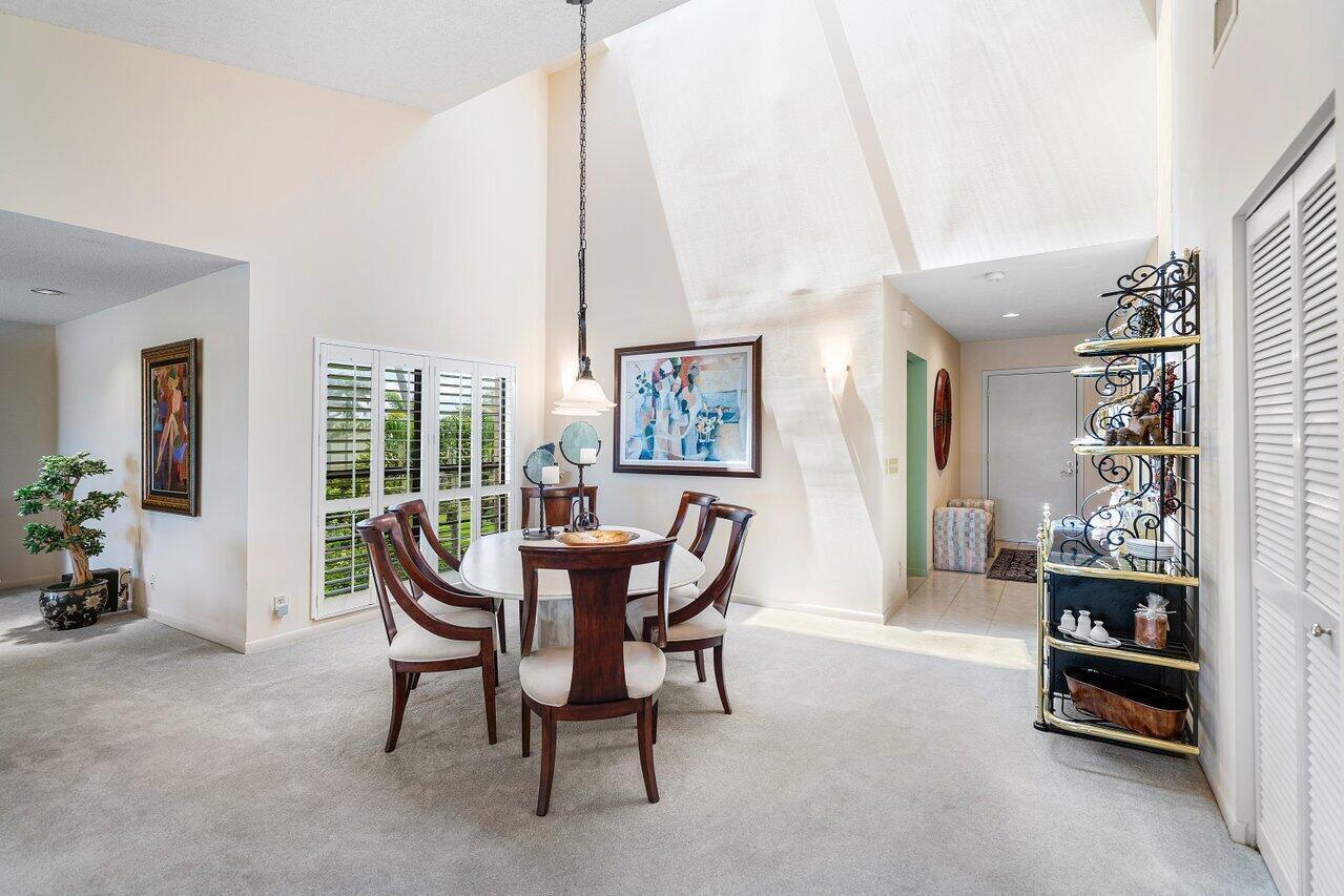 A dining area with a high vaulted ceiling, carpeted floors, and a round wooden table — 69 Eastgate Drive Unit D, Boynton Beach FL 33436, BOYNTON BEACH, FL
