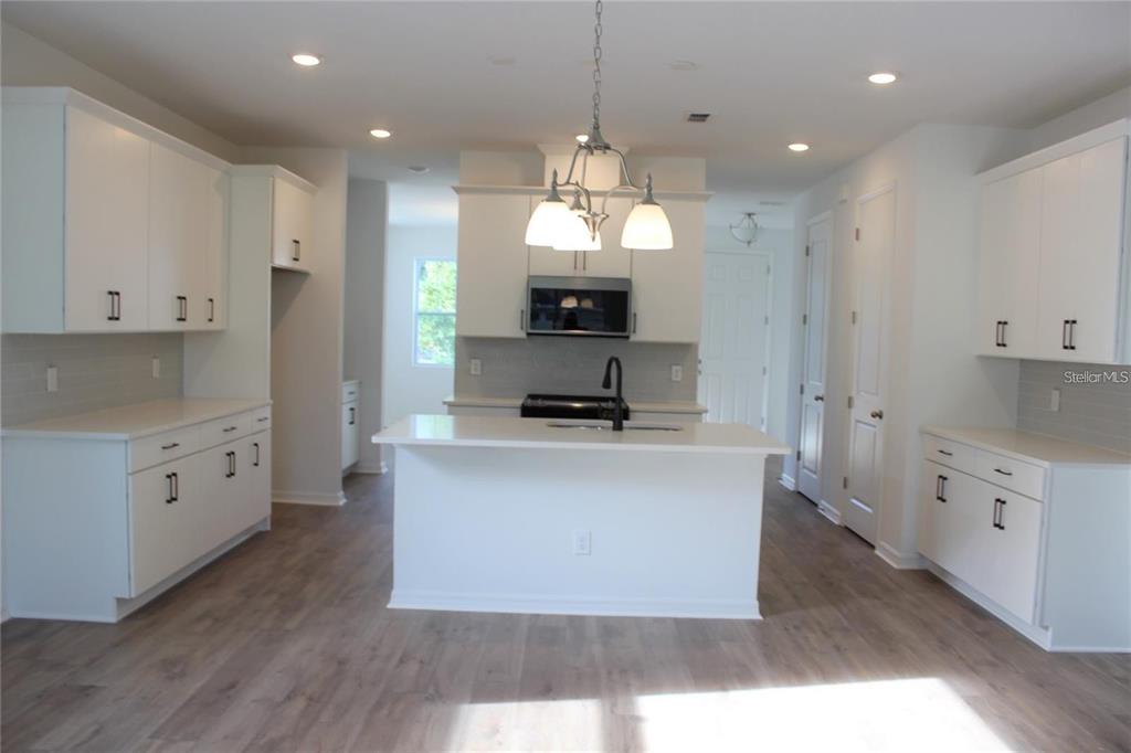 A modern kitchen features white cabinetry, a central island with a sink, and wood-look flooring — 9186 WAVERLY WALK DRIVE, ORLANDO, FL