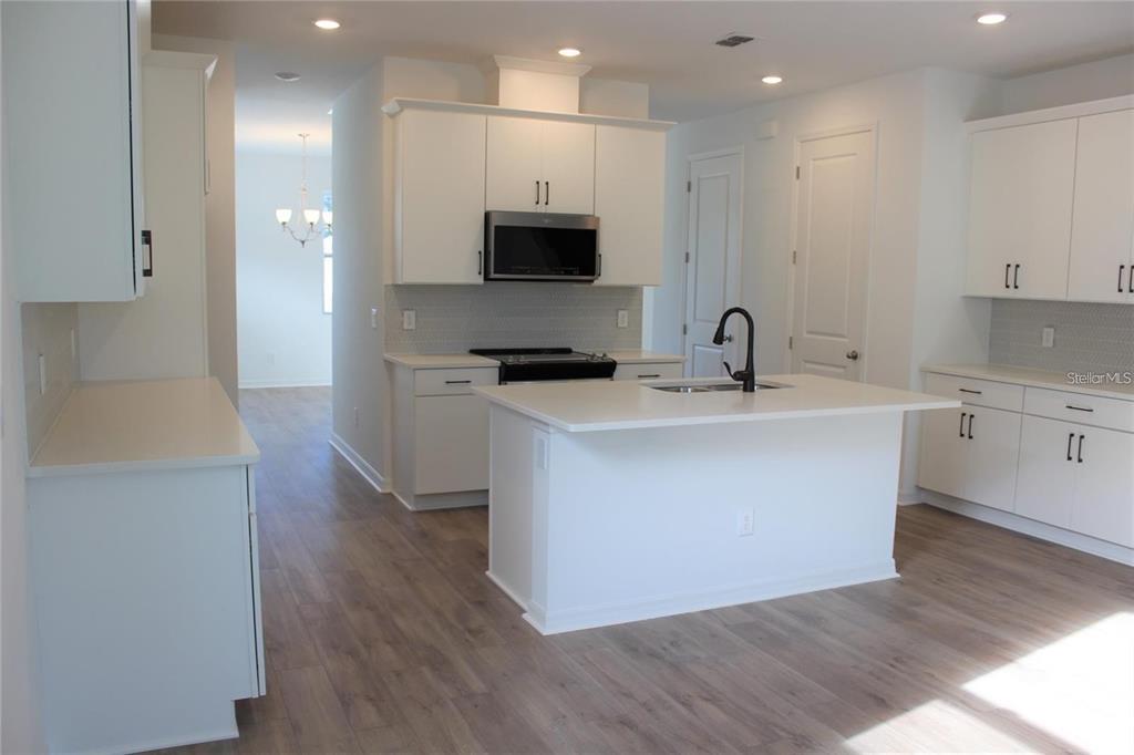 A modern kitchen features white cabinets, a central island with a sink, and wood-look flooring — 9186 WAVERLY WALK DRIVE, ORLANDO, FL