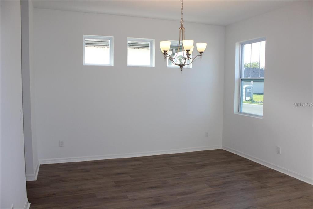 An empty dining room features white walls, dark wood-look flooring, and a hanging chandelier — 9186 WAVERLY WALK DRIVE, ORLANDO, FL