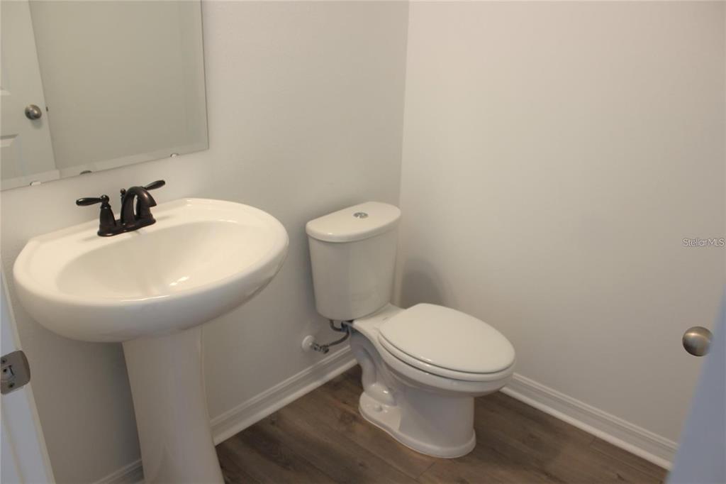 A small bathroom features a white pedestal sink, a toilet, and light wood-look flooring — 9186 WAVERLY WALK DRIVE, ORLANDO, FL