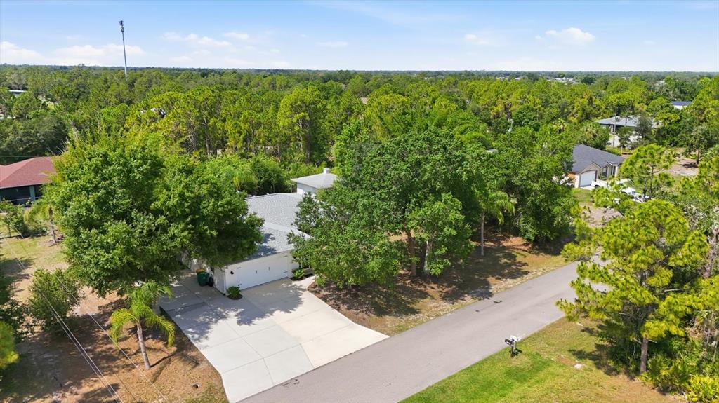 An aerial view shows a house with a white garage and driveway surrounded by trees — 22481 MADELYN AVENUE, PORT CHARLOTTE, FL