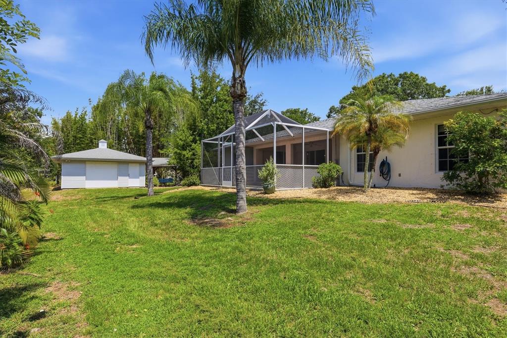 A backyard view of a house with a screened-in patio and a detached garage — 22481 MADELYN AVENUE, PORT CHARLOTTE, FL